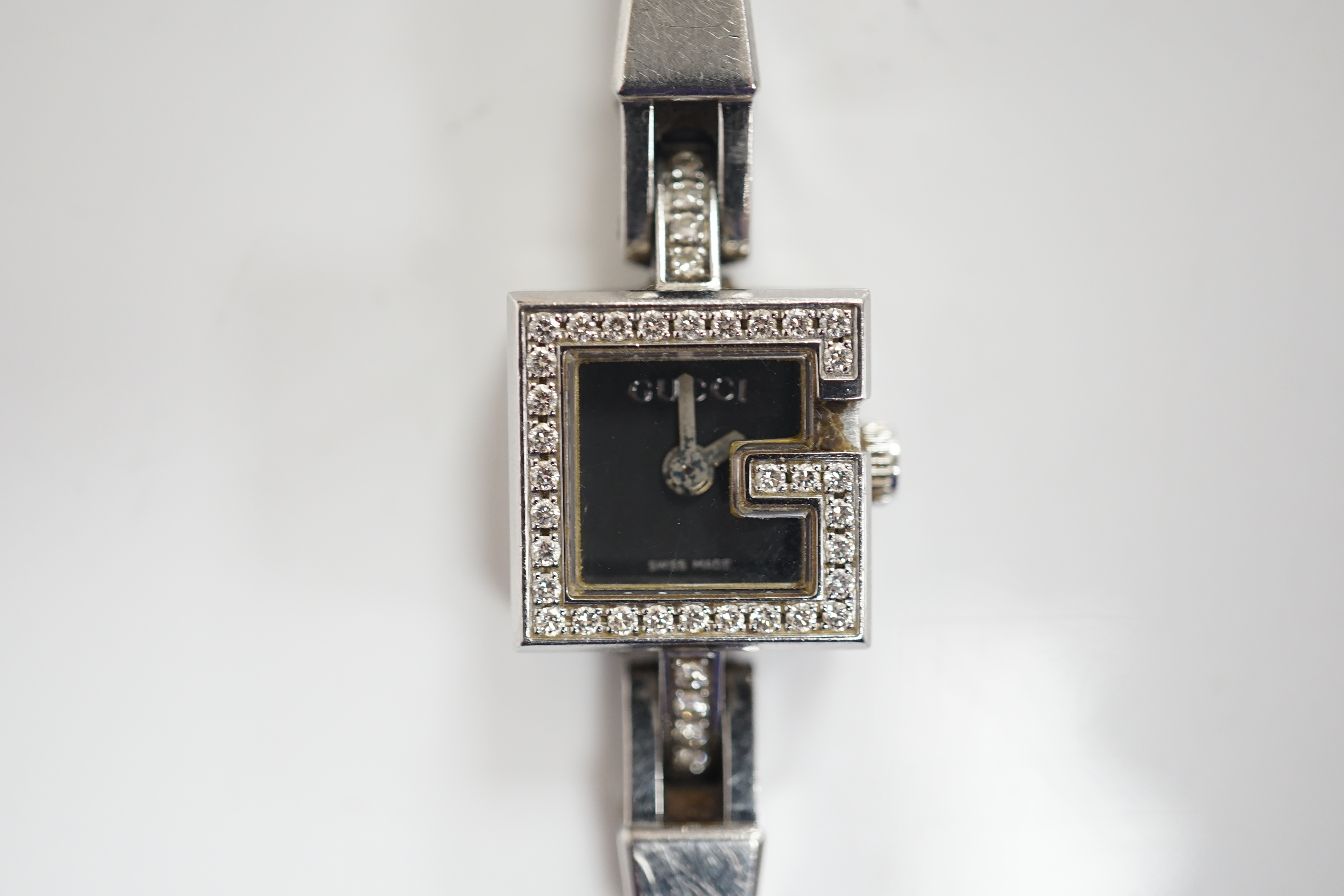 A lady's stainless steel Gucci quartz wrist watch, with G shaped case and diamond chip set bezel, on a stainless steel Gucci bracelet. Condition - fair